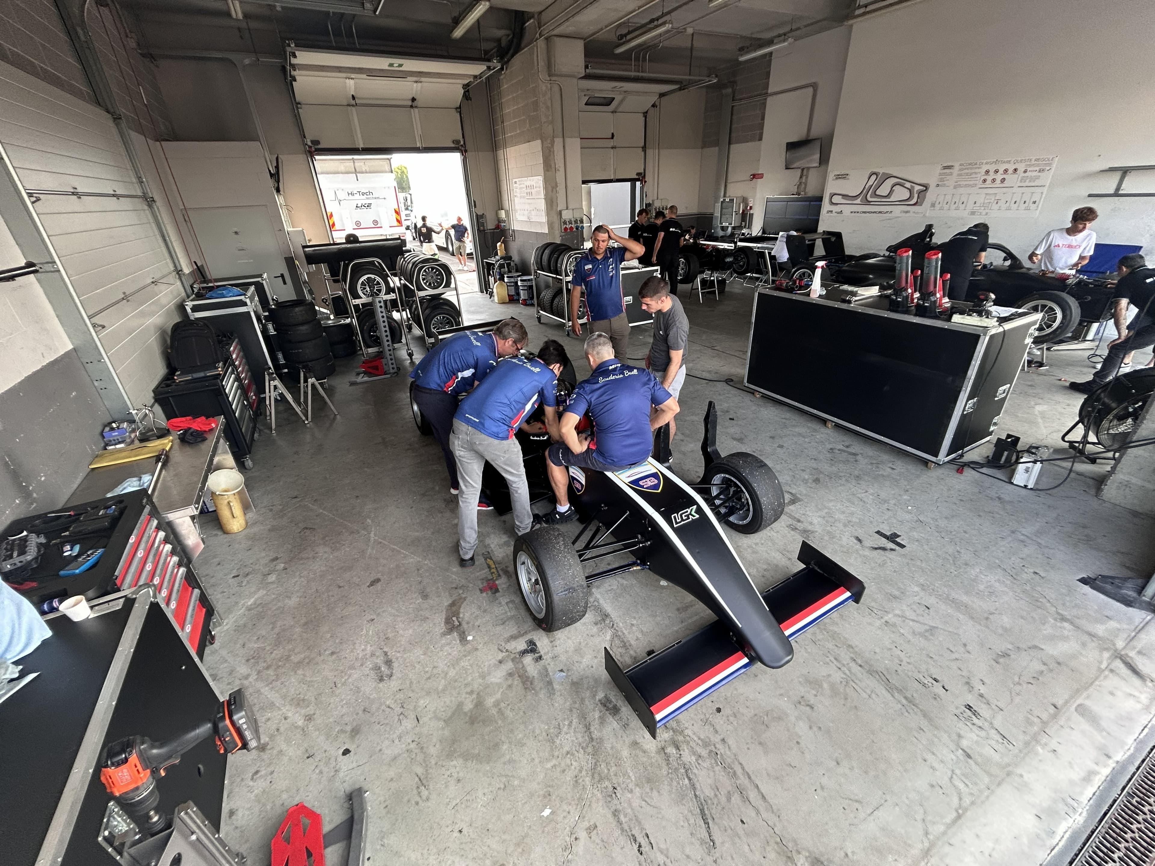 Black formula car in garage with team preparing the car
