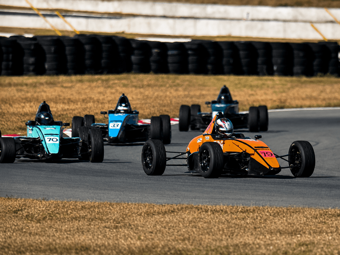 Open-wheel cars racing in traffic with an orange car ahead