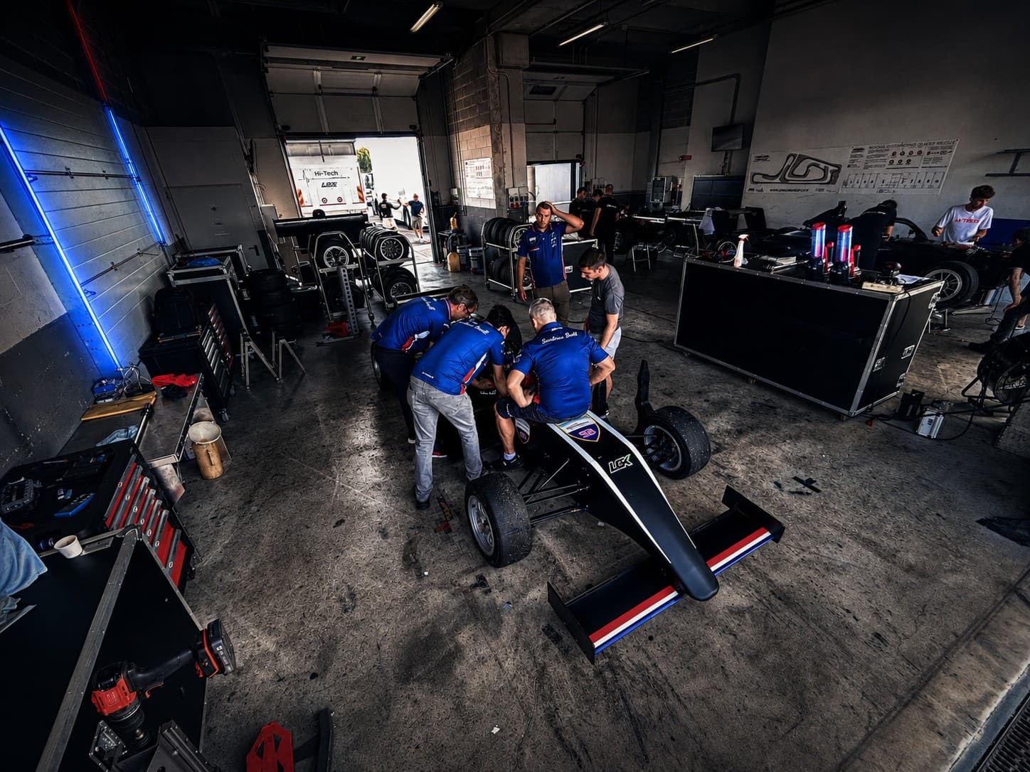 Black formula car in garage with team preparing the car