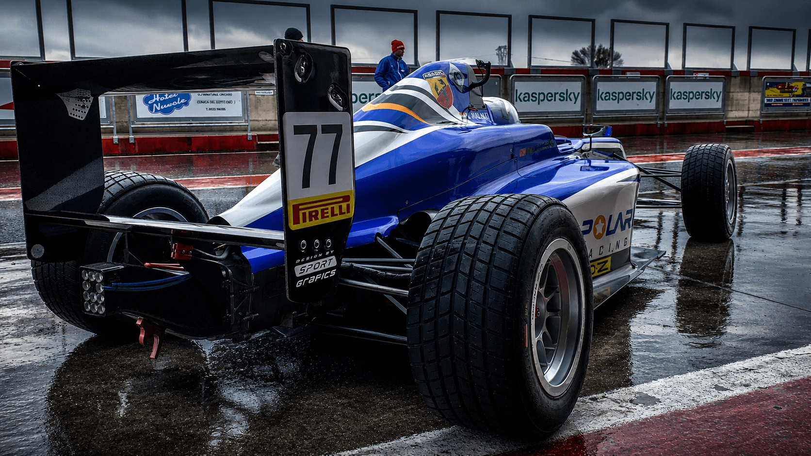 Blue Formula 4 car in a wet pit lane from the rear