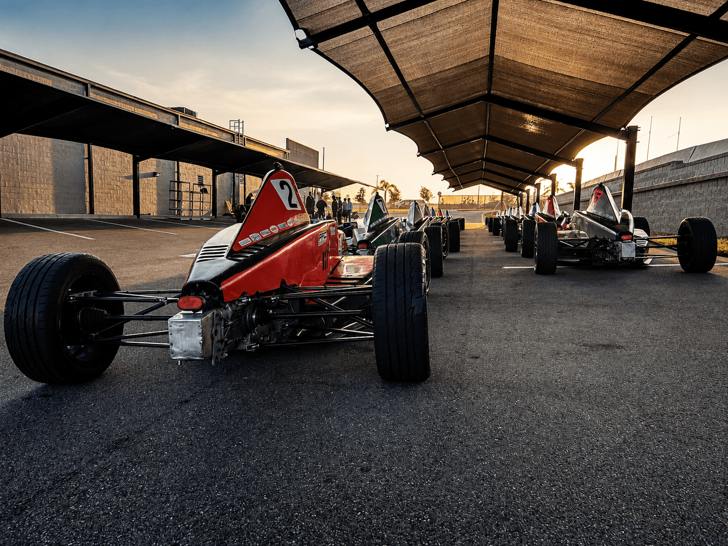 Open-wheel race cars lined up at sunset before track sessions