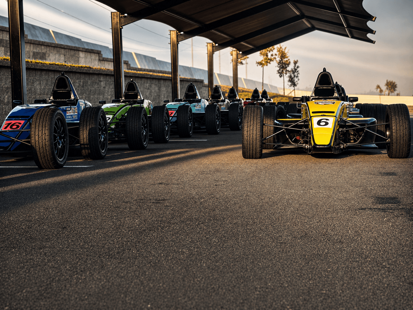 Open-wheel race cars lined up in the paddock before track activity