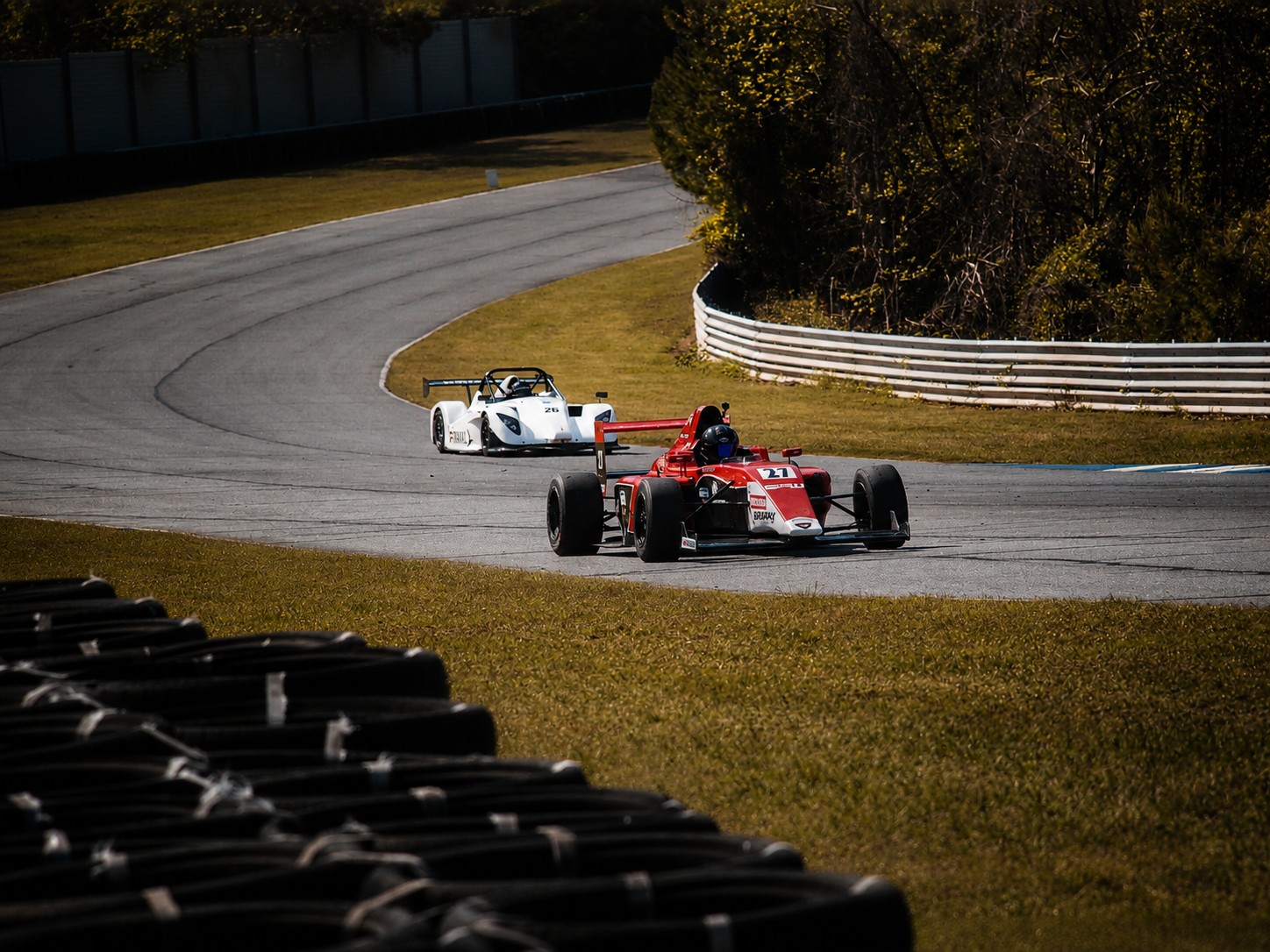 Red formula car followed by a white car on track
